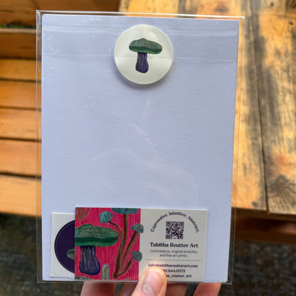 Small, abstract fine art print, held by the artist outdoors by a wooden bench. The back of the print displays a beige sticker with a mushroom and a business card inside the sealed cellophane sleeve to protect the archival inks.