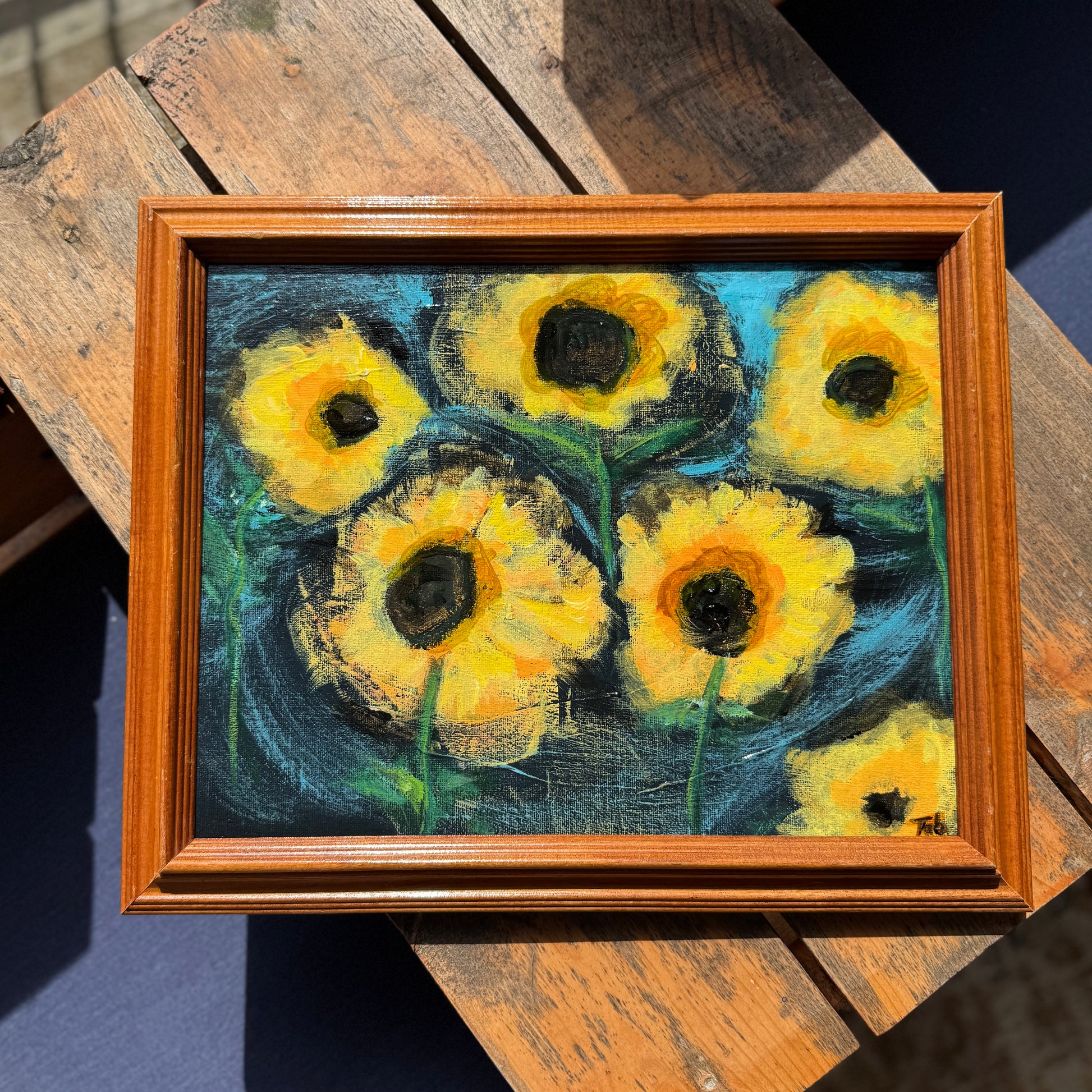 Framed painting of sunflowers on a wooden surface