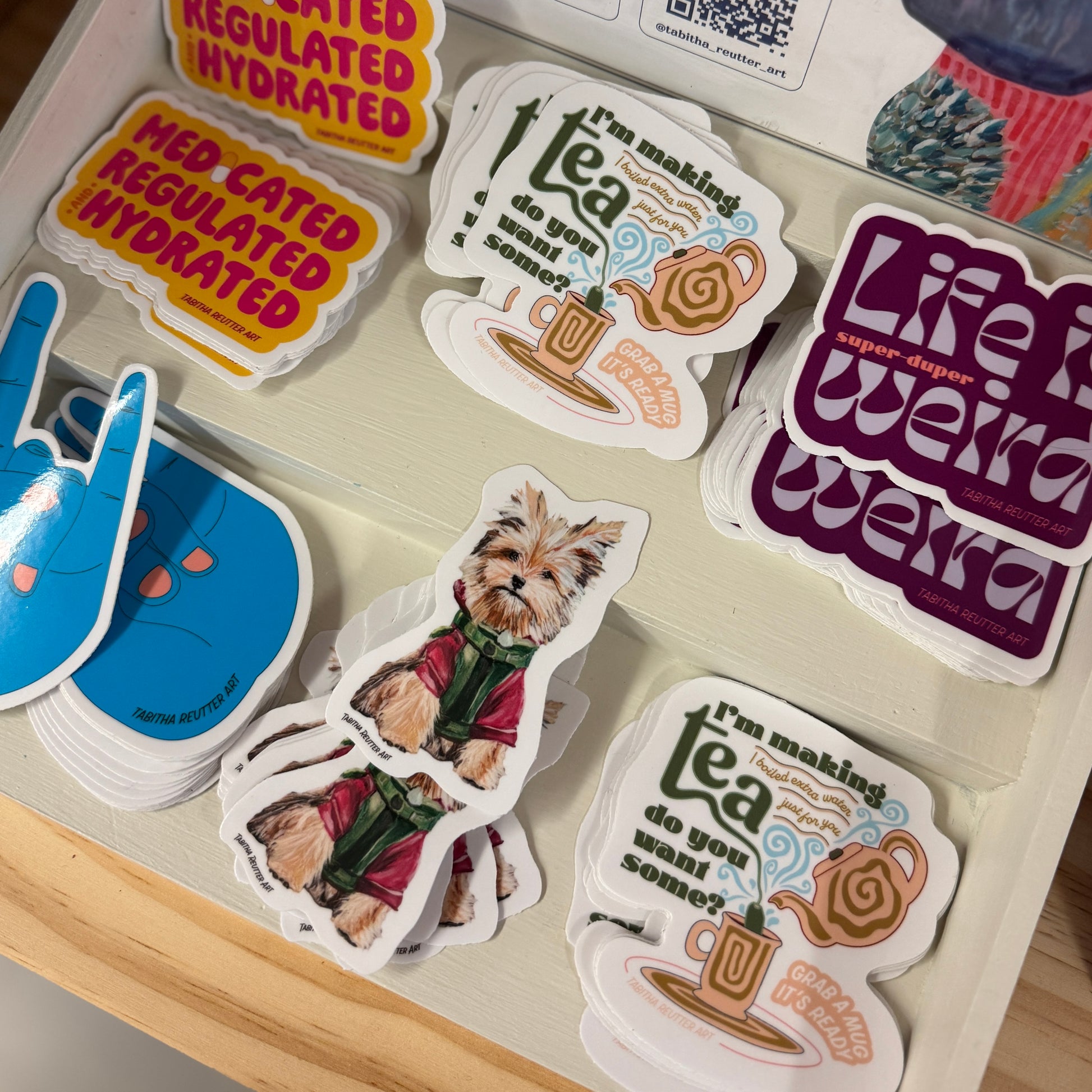 Vinyl stickers on display at Blue Whale Consignment in Seattle, Washington. Stickers are colorful, playful, and feature tea, a dog, a rock and roll hand, and short sayings.