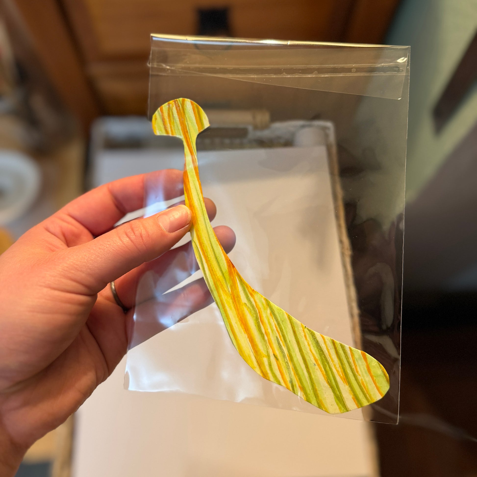 Large handmade art sticker. The sticker is yellow with orange and green stripes with a small mushroom cap and a long, thick stem.